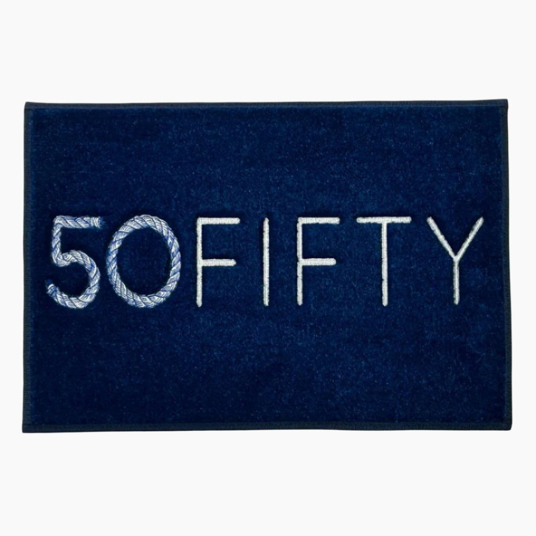 A navy blue marine carpet boat mat with the word '50FIFTY' embroidered in white. Custom embroidered logo mat for luxury yacht dock