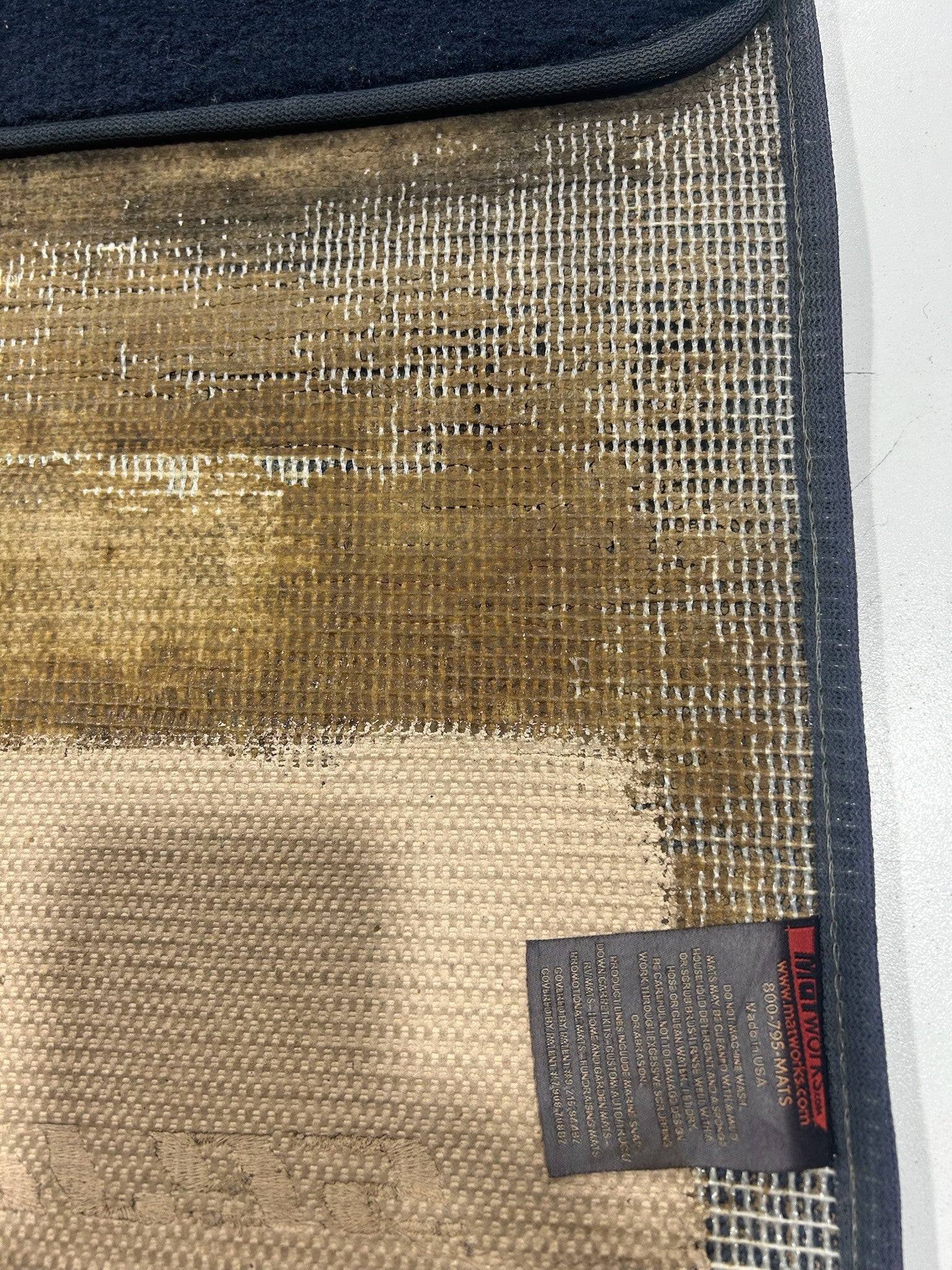 Close-up of competitor mat backing disintegrating with exposed mesh and deteriorating edging