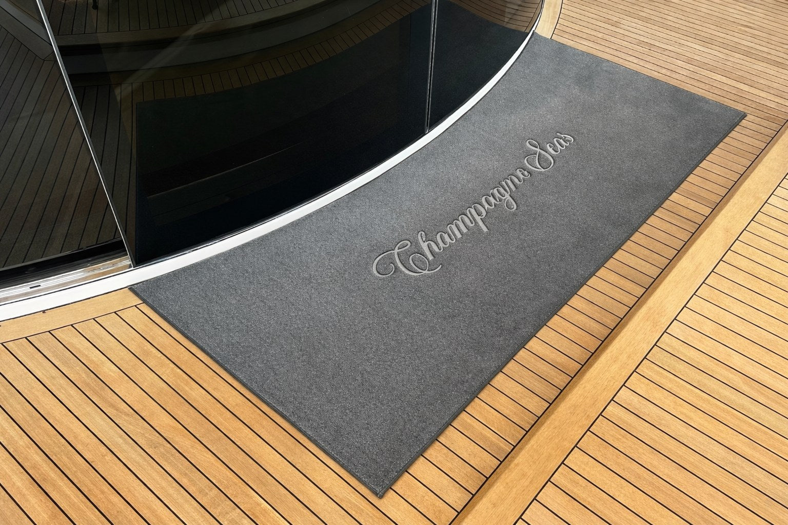 Custom embroidered deck mat on teak deck with curved glass yacht door