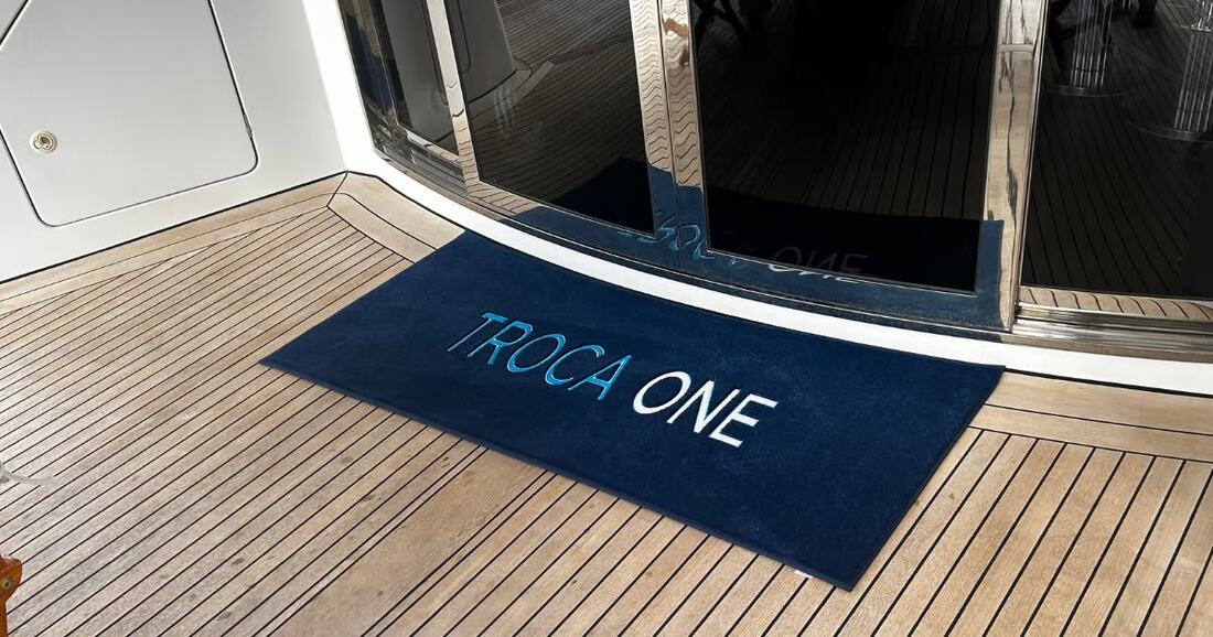 Custom yacht mat reading TROCA ONE at a motor yacht's glass aft doors
